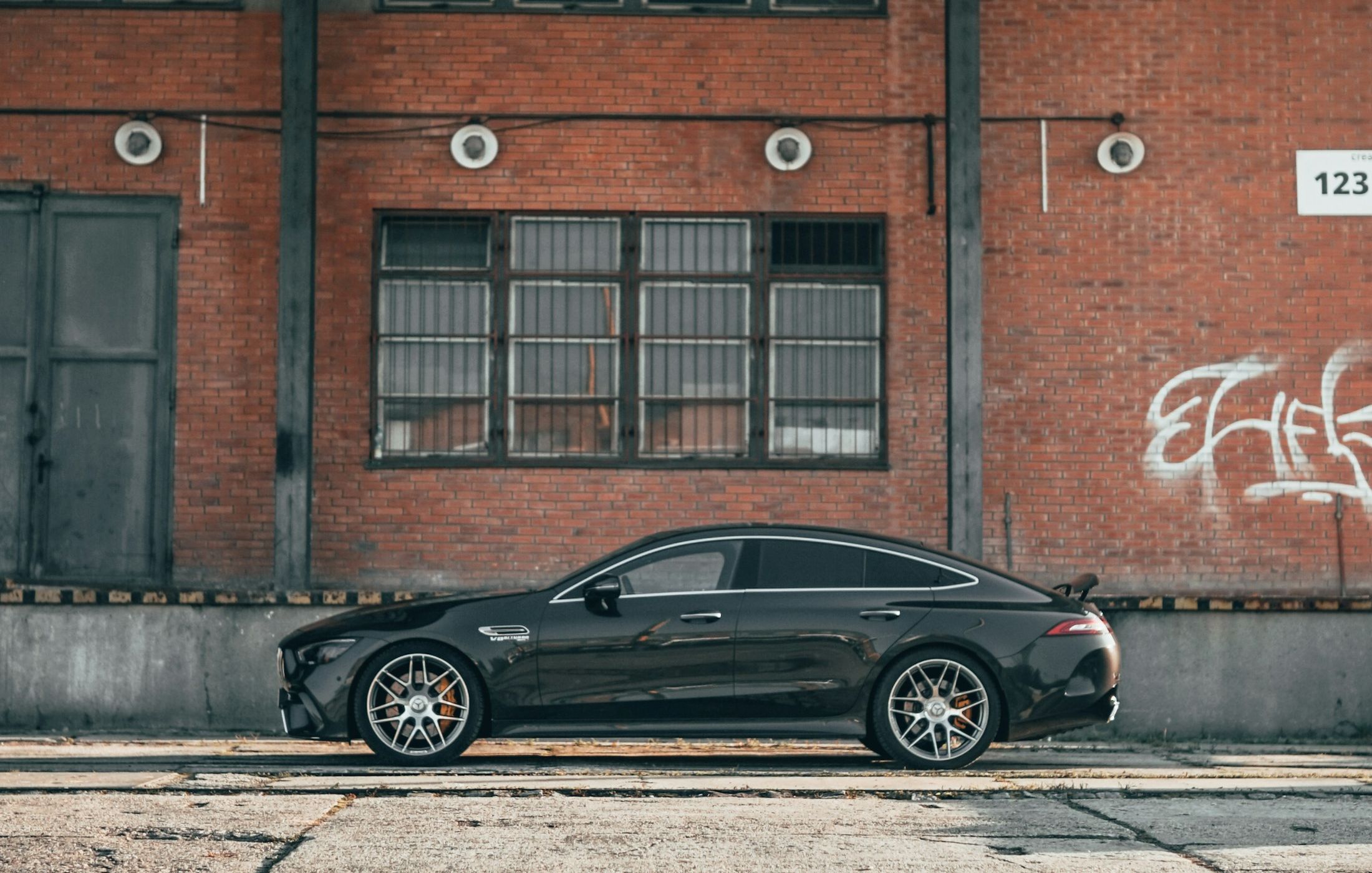 Mercedes-AMG GT 63 S negru, profil complet, în fața unei clădiri industriale