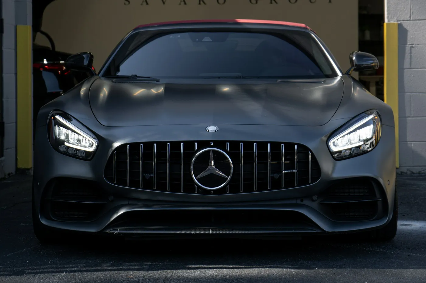Mercedes-AMG GT, vedere frontală, vopsea mată, faruri aprinse în pragul unui atelier
