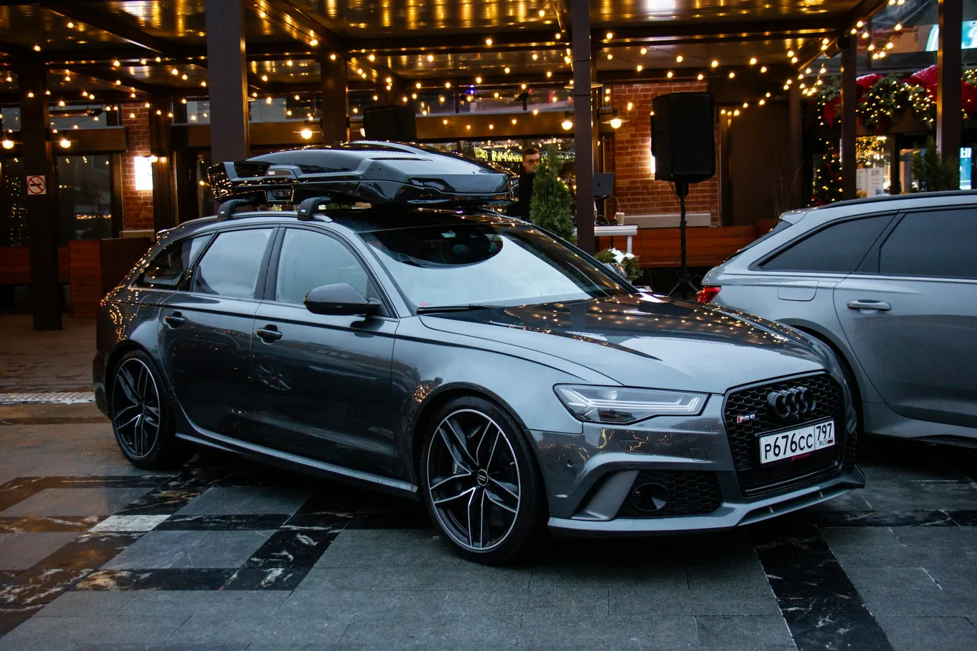 Audi RS6 Avant gri închis, parcat seara lângă o terasă luminată